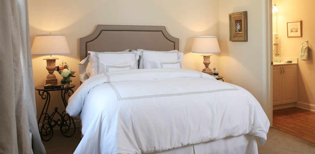 A cozy bedroom with a neatly made bed and a bedside lamp.