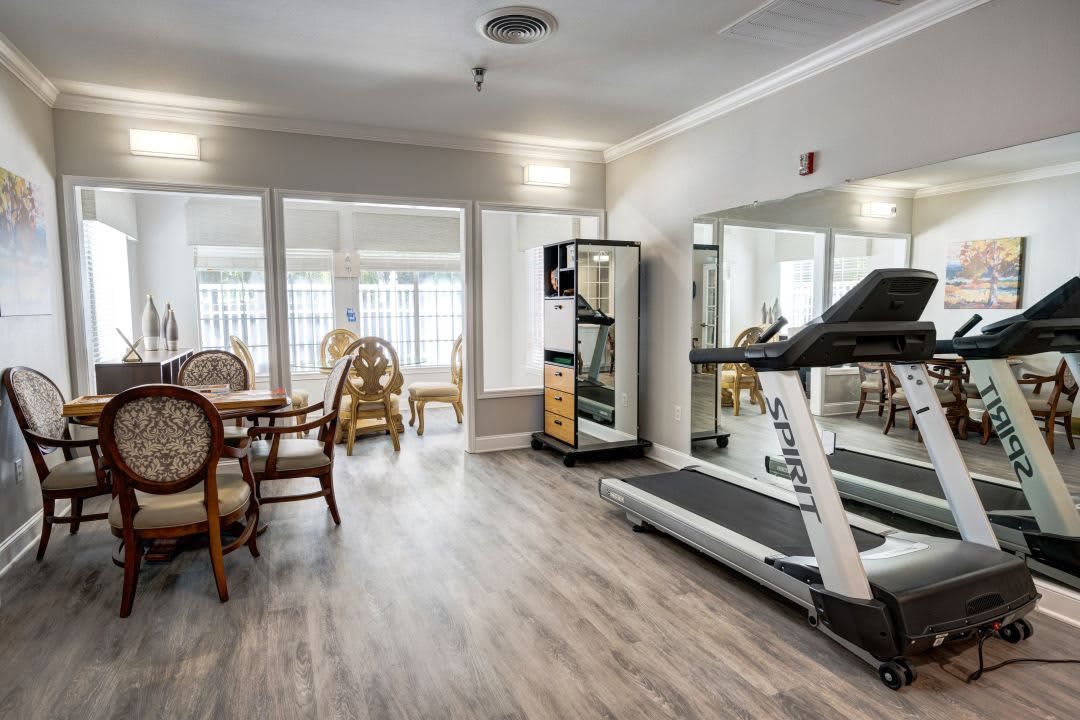A small gym with a treadmill, mirrors, and a seating area.
