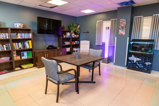 A modern workspace featuring a table and chairs, equipped with shelves and a television for meetings.