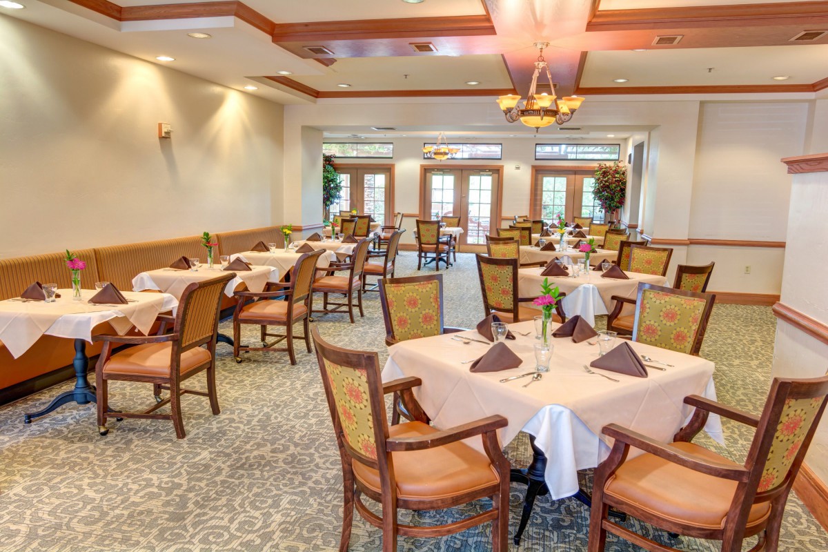 An elegant dining room with neatly arranged tables and chairs, featuring a decorative chandelier.