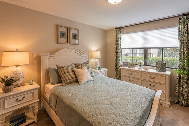 A cozy, well-decorated bedroom with a large bed, two nightstands, lamps, and a dresser by the window.