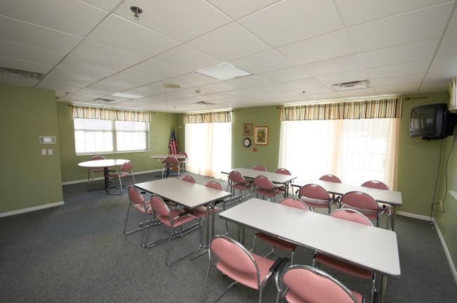 A conference room with several pink chairs around white tables, illuminated by natural light from large windows.