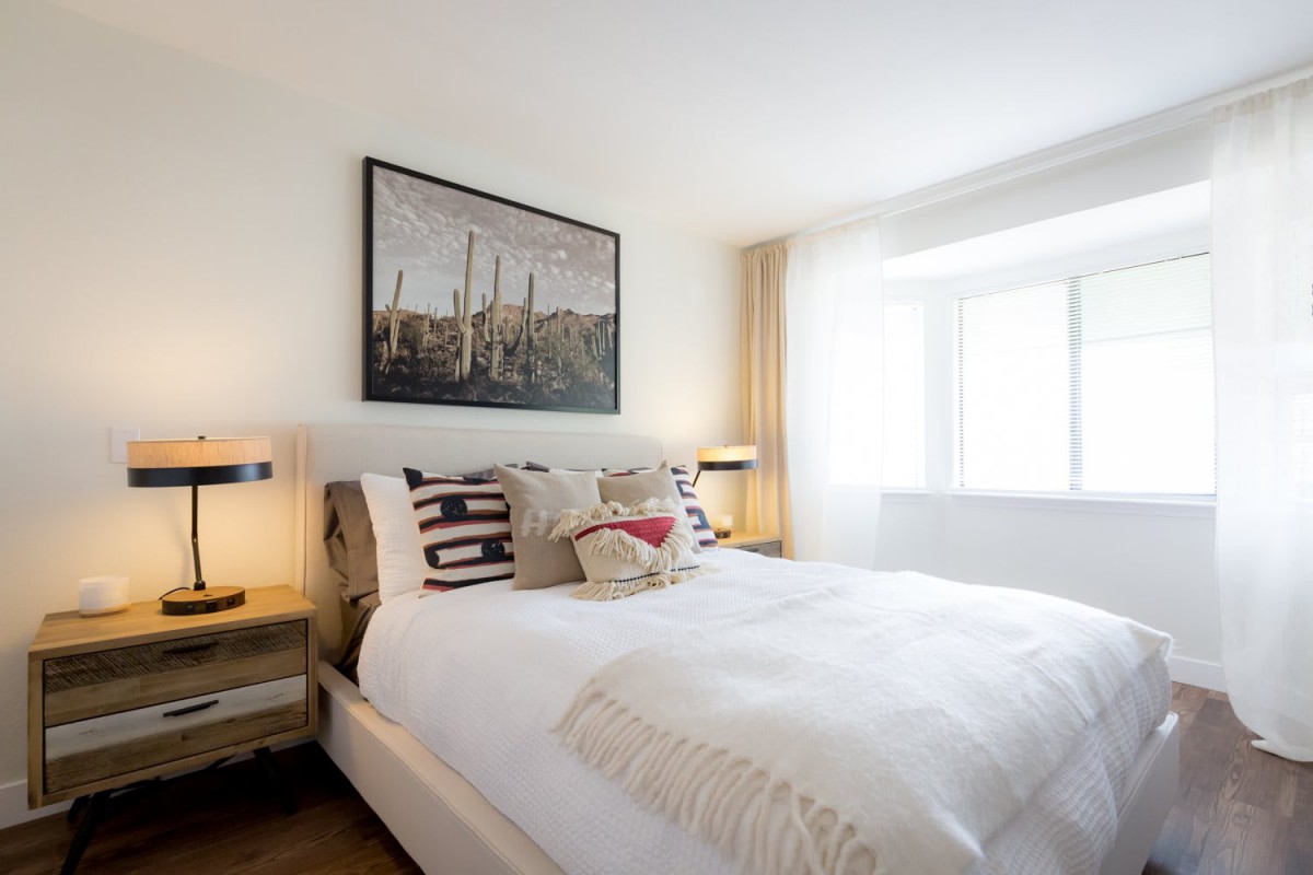 A modern bedroom with natural lighting and stylish decor, featuring white bedding and wall art.