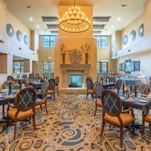 An elegant restaurant dining area with a central chandelier, carpeted floor, and a fireplace.