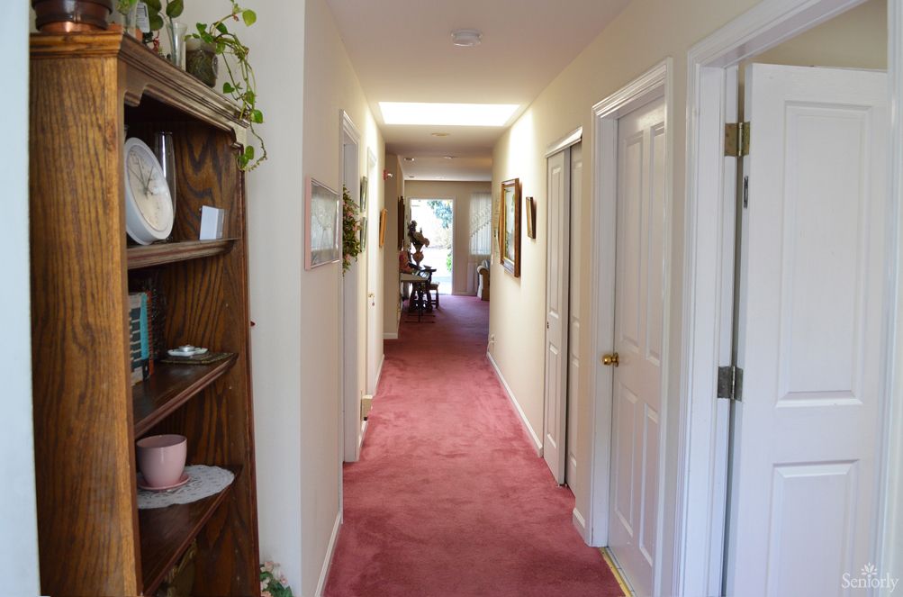A long carpeted hallway with doors and shelves on the sides.