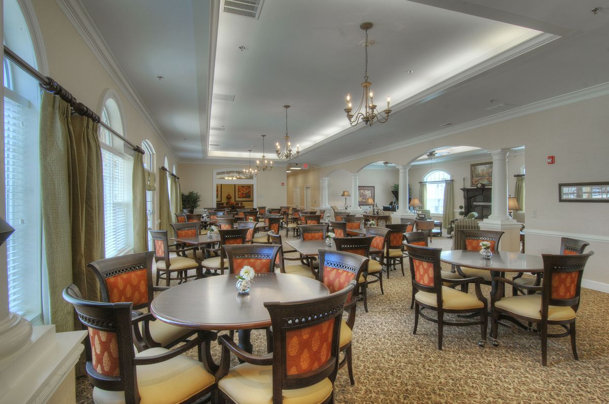 A spacious dining area with elegantly arranged tables and chairs, featuring chandeliers and a warm interior design.