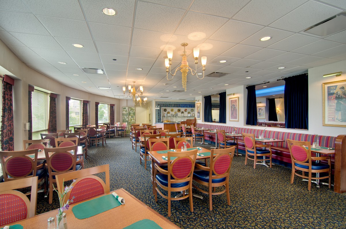 An empty restaurant dining room with neatly arranged tables and chairs, illuminated by chandeliers.