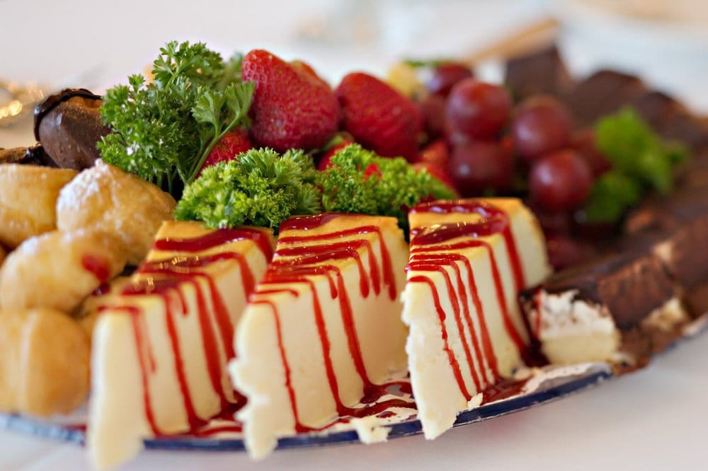 A platter of cheesecake slices drizzled with sauce, garnished with strawberries and grapes.