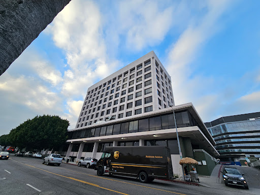 A modern multi-story building against a backdrop of cloudy skies, with vehicles parked along the street.