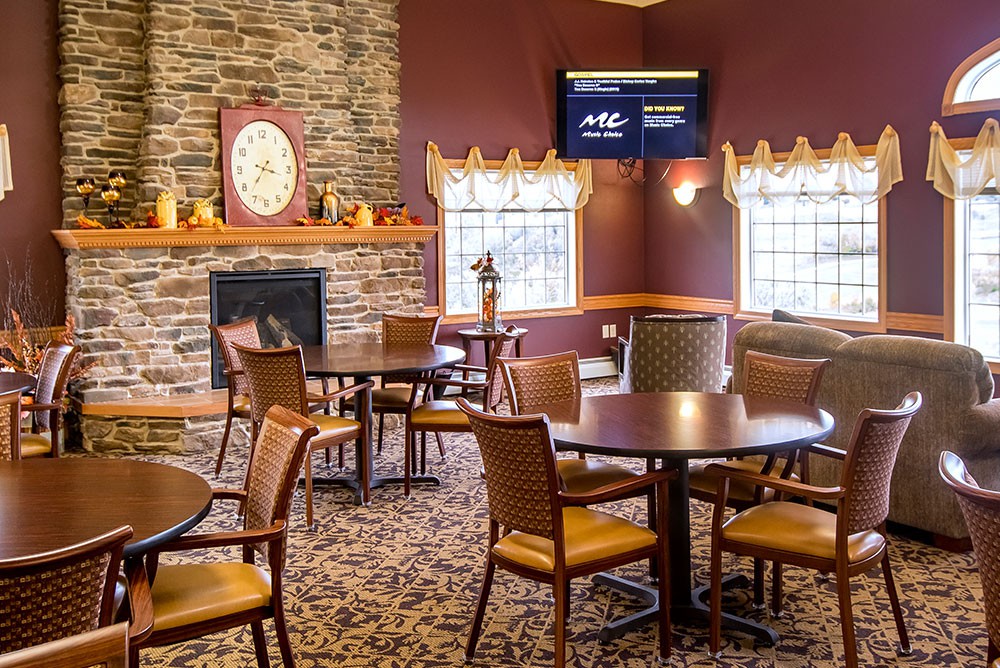 A cozy restaurant interior featuring a fireplace, several tables and chairs, and a wall-mounted television.