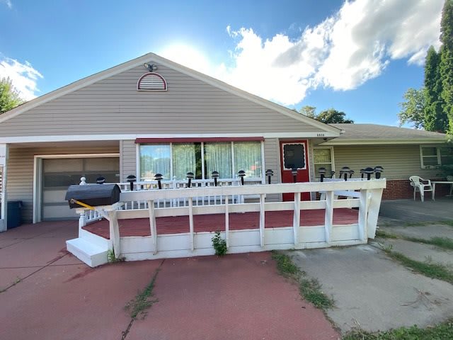 A single-story house featuring a front porch with a white ramp and railing under a partly cloudy sky.