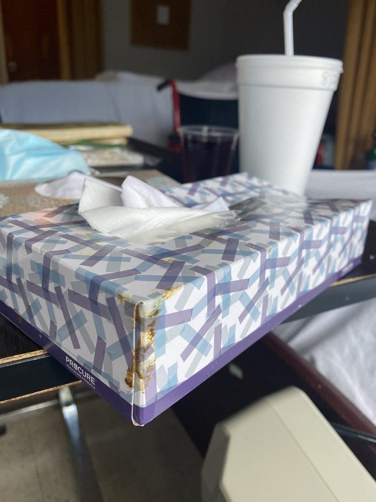 A tissue box and a cup on a cluttered table.