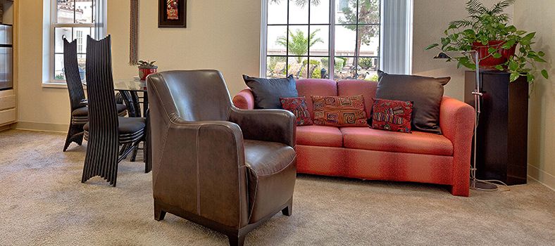 A cozy living room featuring a leather chair and a red sofa, with a large window letting in natural light.