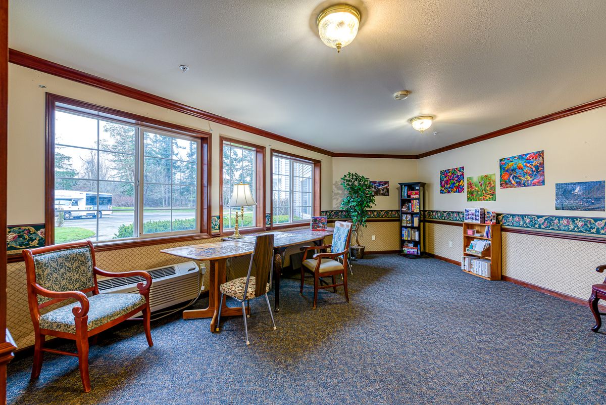 A cozy interior room featuring a large table, several chairs, and a bookshelf with ample natural light from multiple windows.