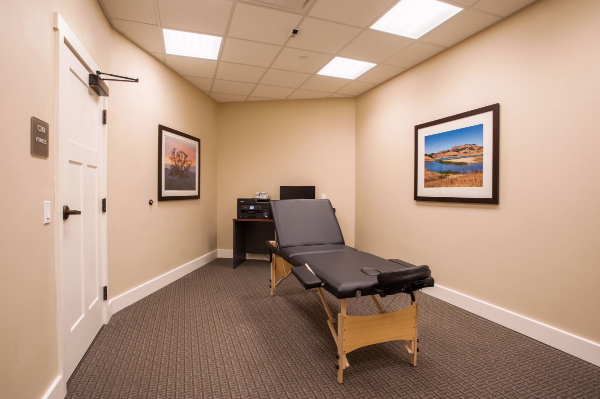 A chiropractic treatment room with a massage table and framed artwork on the walls.