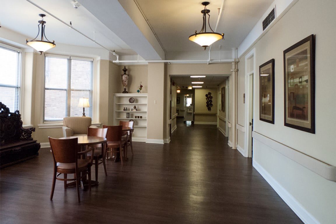 A well-lit hallway with a small dining area featuring tables and chairs, hardwood flooring, and decorative lighting.