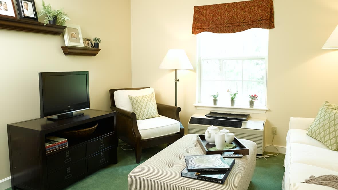 A cozy living room with a TV, armchair, and natural light from a window.