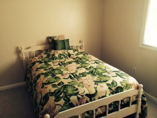 A cozy bedroom with a single bed adorned with green and white floral bedding.