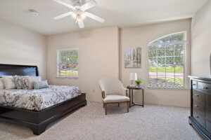 A cozy bedroom with a large bed, upholstered chair, and ample natural light from large windows.