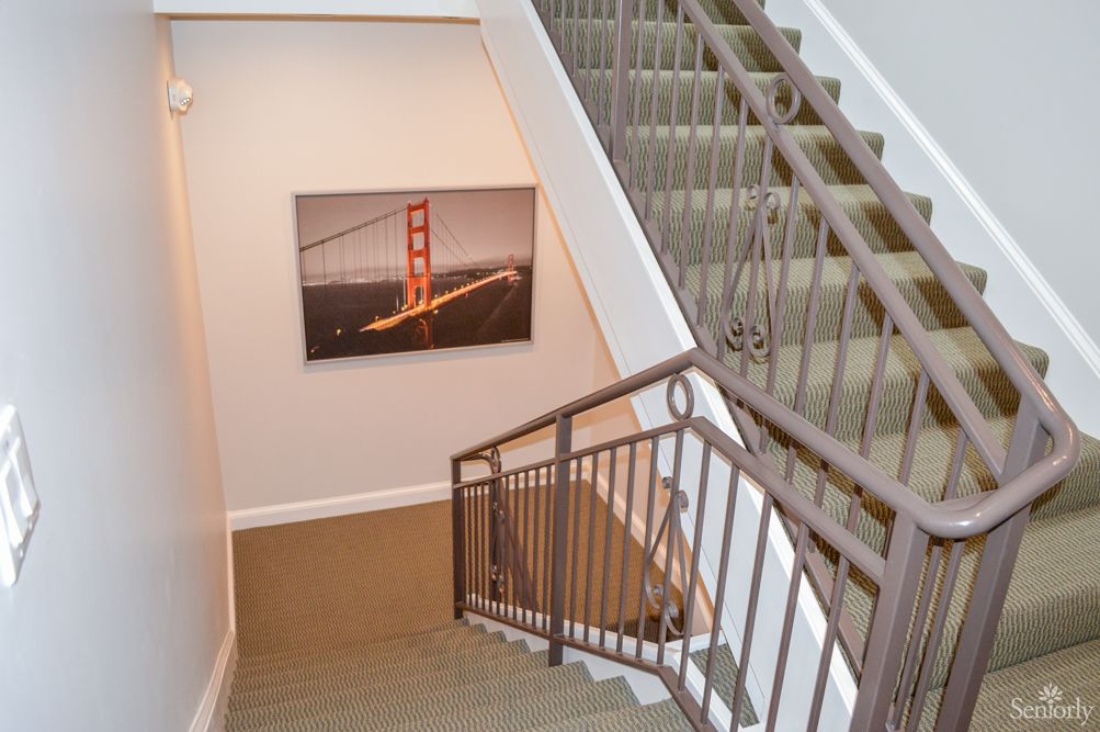 A staircase with carpeted steps and metal handrails, featuring artwork of a bridge on the wall.