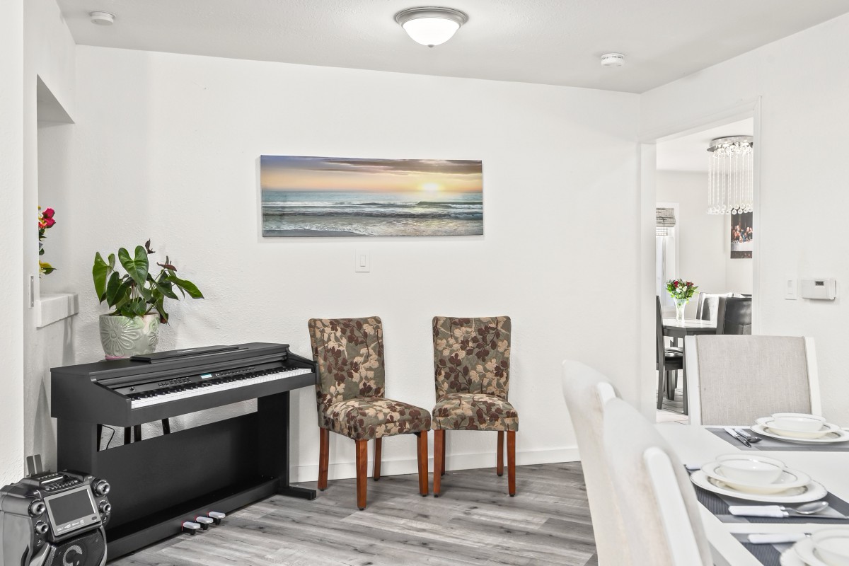 A dining area featuring a piano, two patterned chairs, and a seascape wall art.