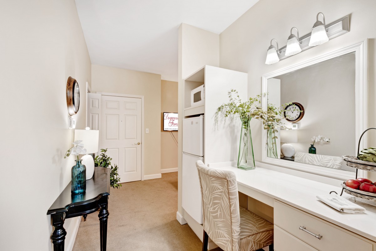 A neatly arranged bedroom corner with a desk, chair, and mirror, adorned with decorative elements like vases and framed artwork.
