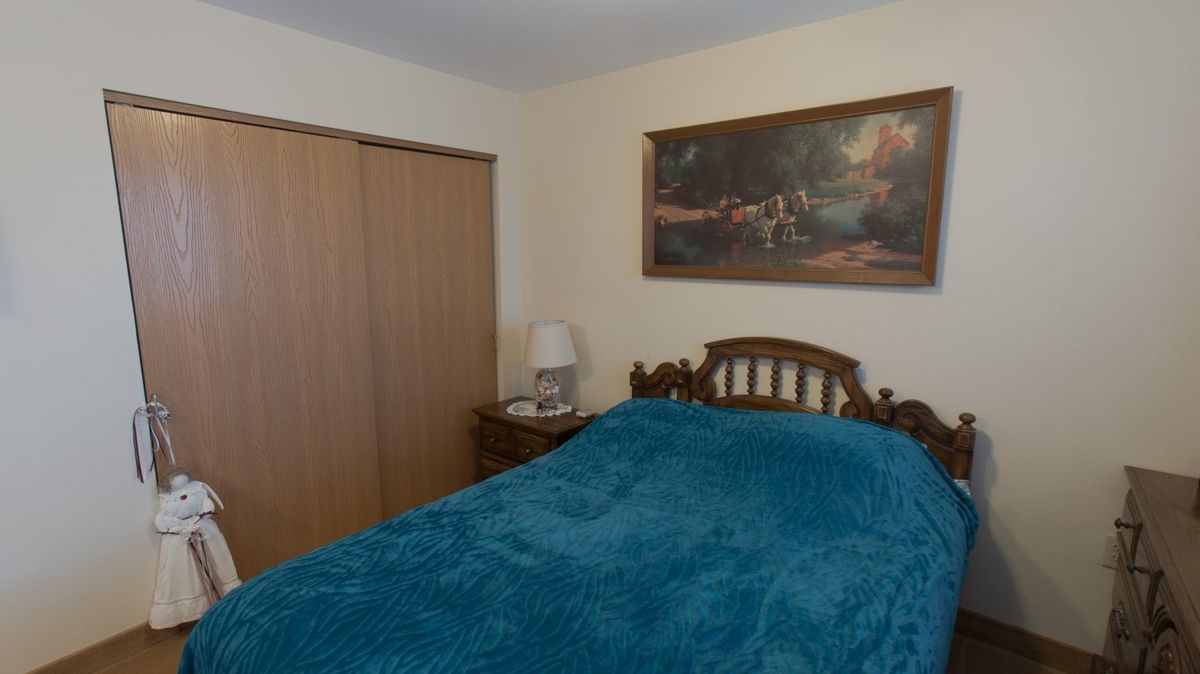 A cozy bedroom featuring a wooden bed with teal bedding, a bedside lamp, and a painting on the wall.