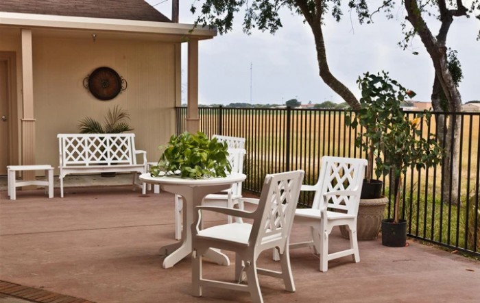 A cozy patio with white outdoor furniture and a potted plant in a garden setting.