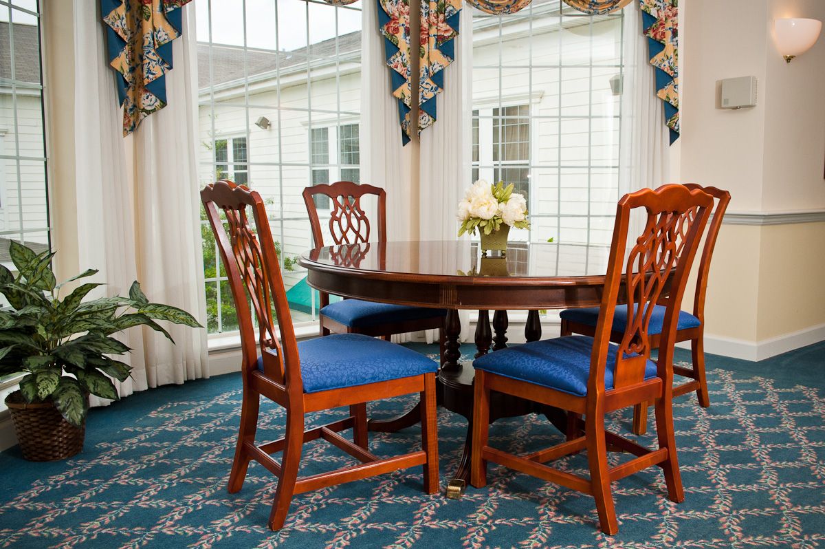 A cozy dining room with a wooden table and chairs, featuring large windows and patterned curtains.