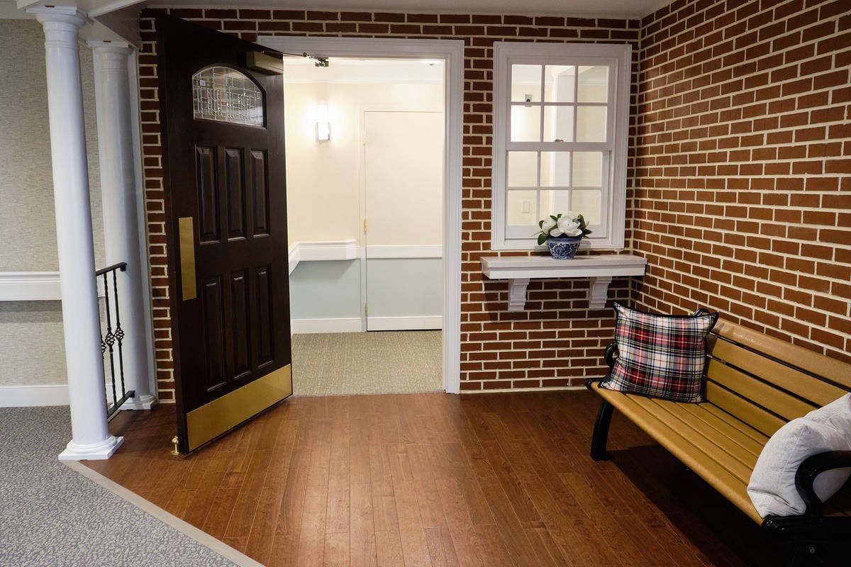 A cozy interior space with a brick wall, open door, and wooden bench adorned with cushions.