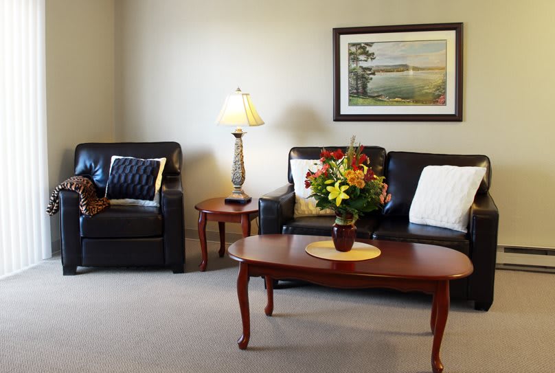 A cozy living room with leather sofas, a coffee table adorned with a floral arrangement, and soft lighting from a nearby lamp.
