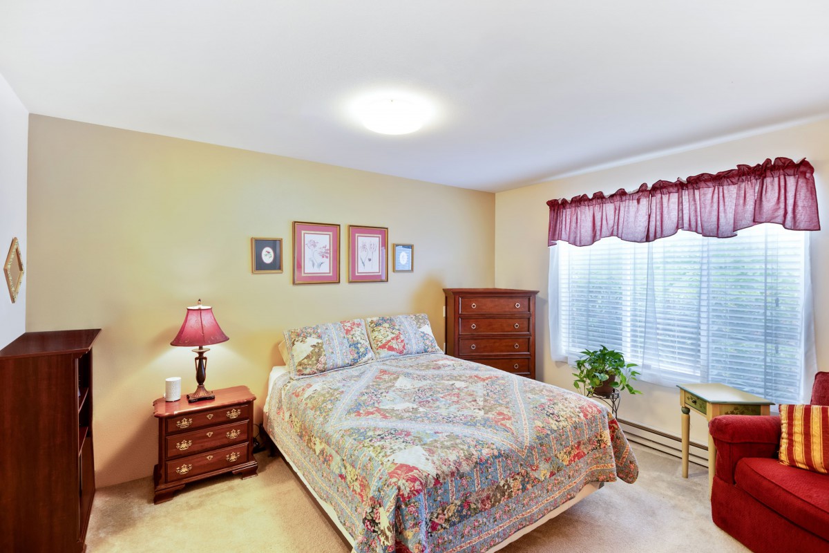 A cozy bedroom with a neatly made bed, wooden furniture, and a window with red curtains.