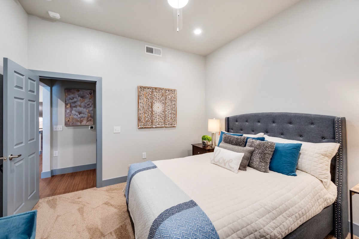 A modern bedroom featuring a cozy bed with decorative pillows, artwork on the wall, and a bedside lamp.