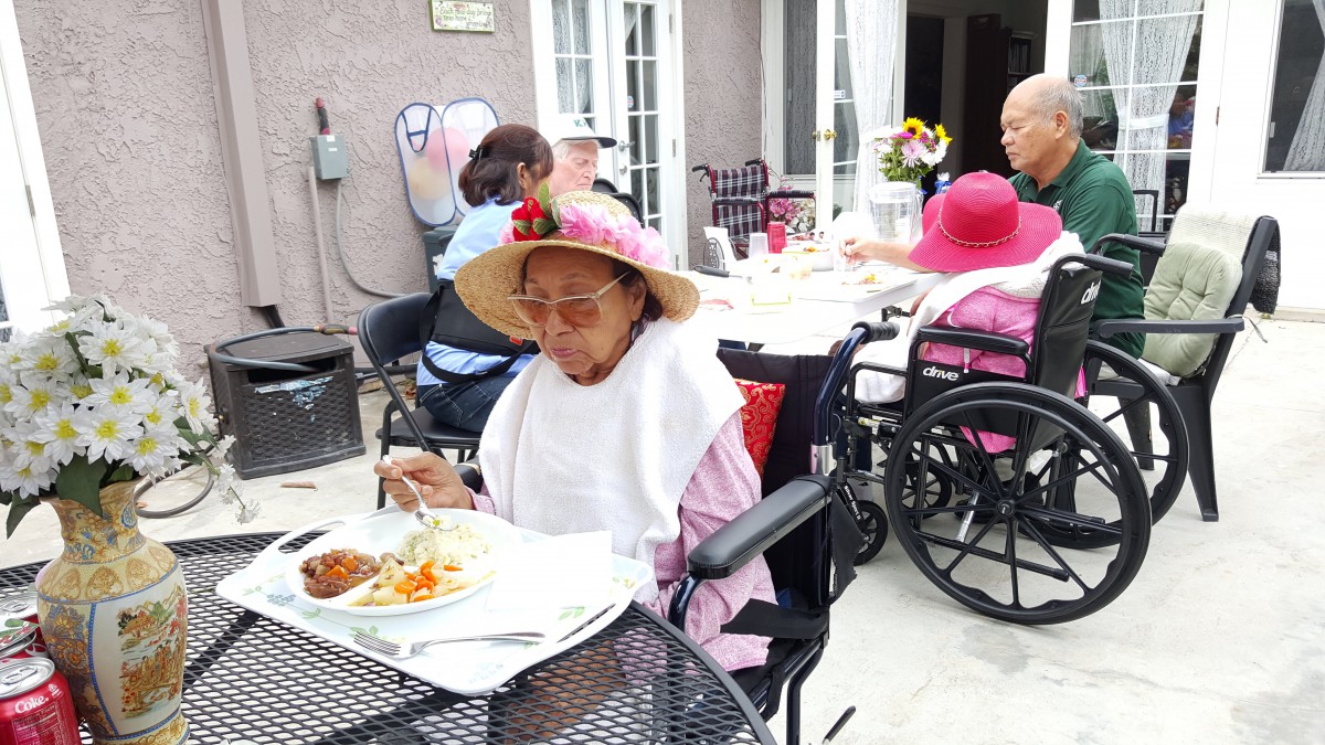 Elderly individuals enjoying a meal outdoors at a social gathering in a nursing home.