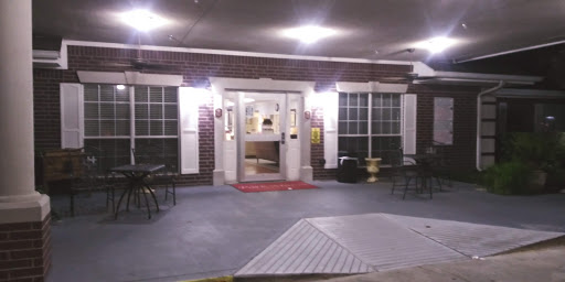 A well-lit entrance to a building at night, featuring large windows and outdoor seating.