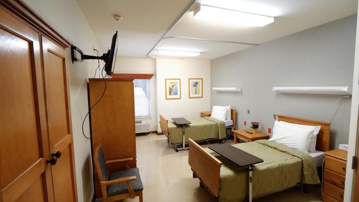 A hospital room with two beds, a television, and chairs.