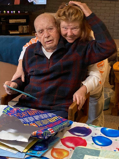 A heartwarming moment between an elderly man and a woman, sharing smiles and warmth over some colorful items on the table.