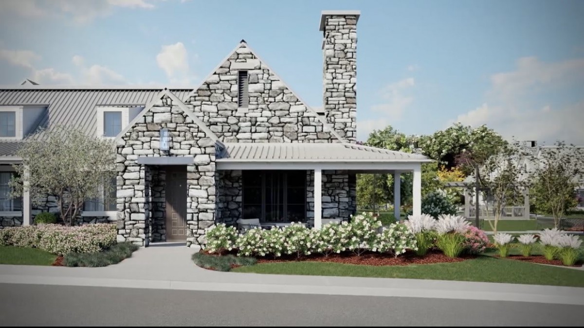 A charming house with a stone exterior, featuring a chimney and a porch surrounded by well-maintained landscaping and flowers.