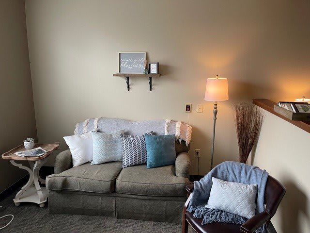 A cozy living room with a sofa, cushions, lamp, and decorative shelf.