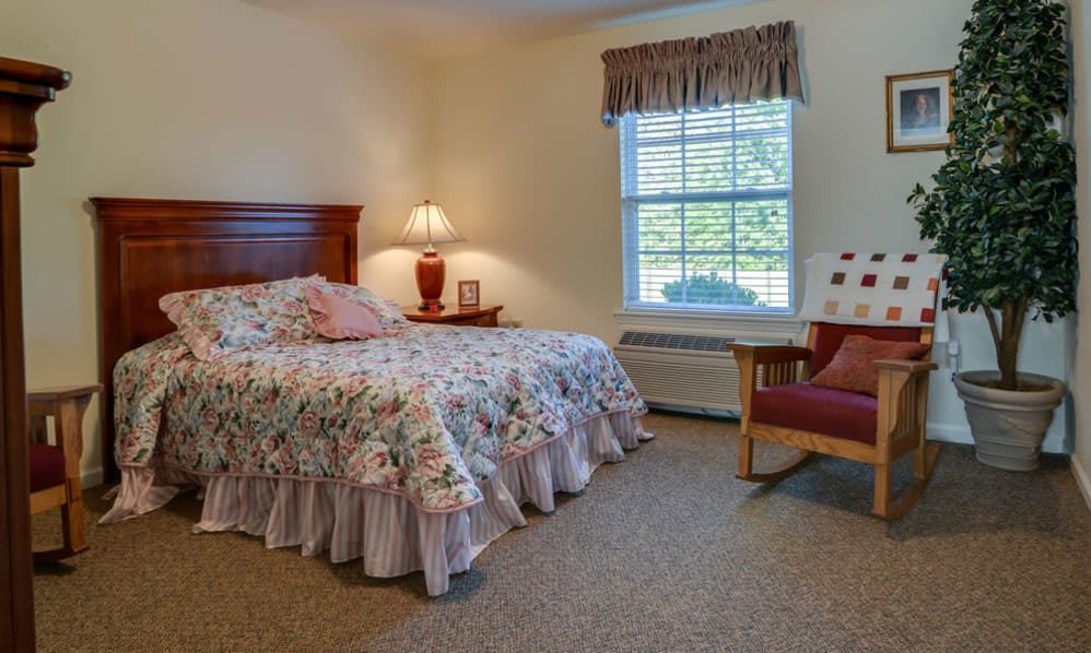 A cozy bedroom featuring a neatly made bed, a bedside lamp, and a comfortable chair near the window.