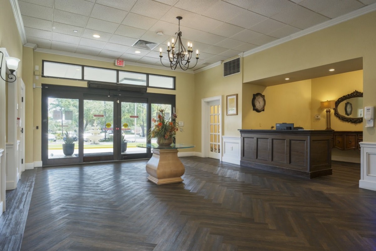 A spacious hotel lobby with a chandelier, wooden floors, and a welcoming front desk.