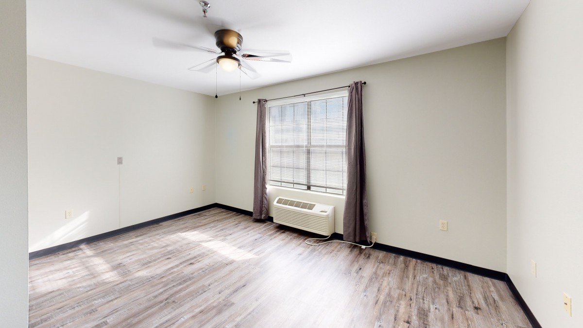 A minimalistic empty room featuring hardwood flooring, a ceiling fan, and a window with curtains.