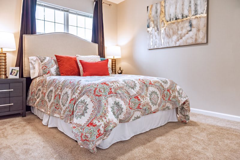 A cozy bedroom with a patterned bedspread, decorative pillows, and wall art.