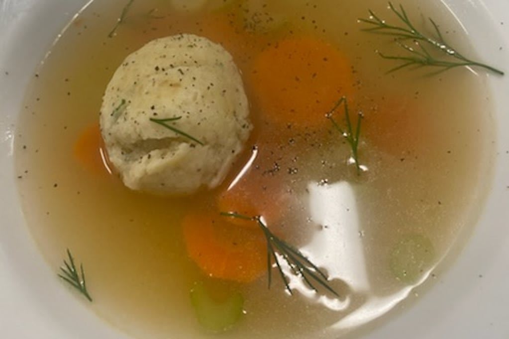 A bowl of matzo ball soup with carrots, celery, and dill.