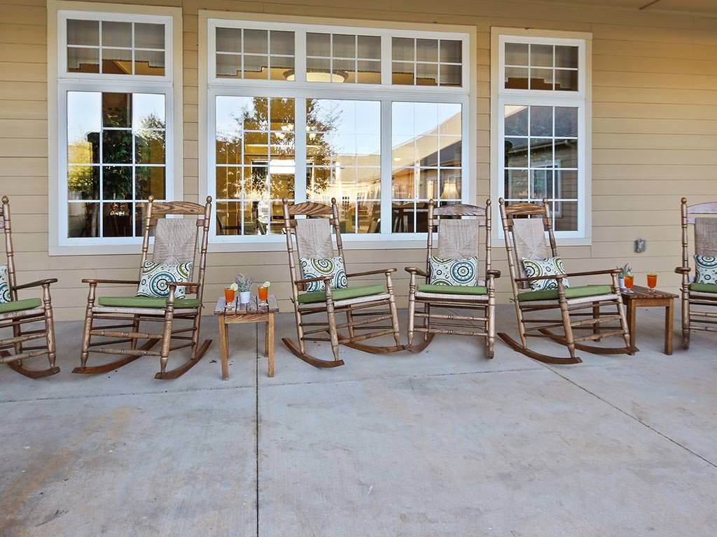 A row of rocking chairs on a patio in front of large windows.