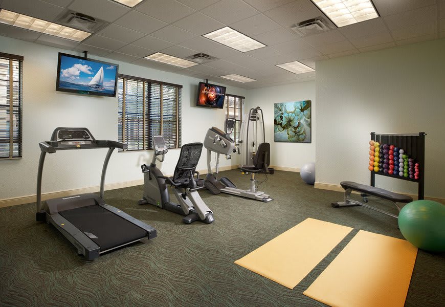 A well-equipped indoor gym space with various fitness machines and televisions.
