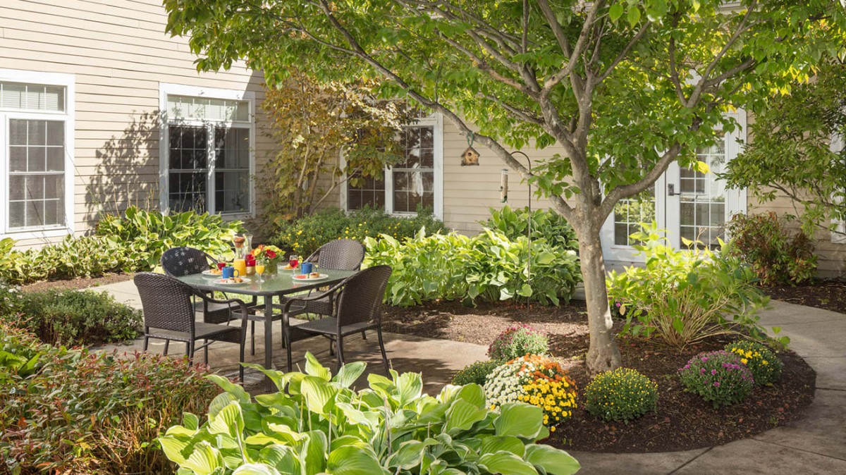 A tranquil garden patio with a table and chairs surrounded by lush greenery and trees.