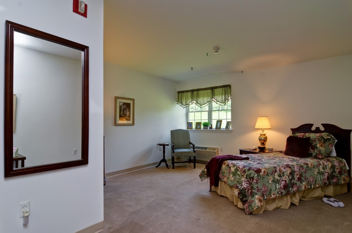 A cozy bedroom with a bed, chair, and lamp near a window.