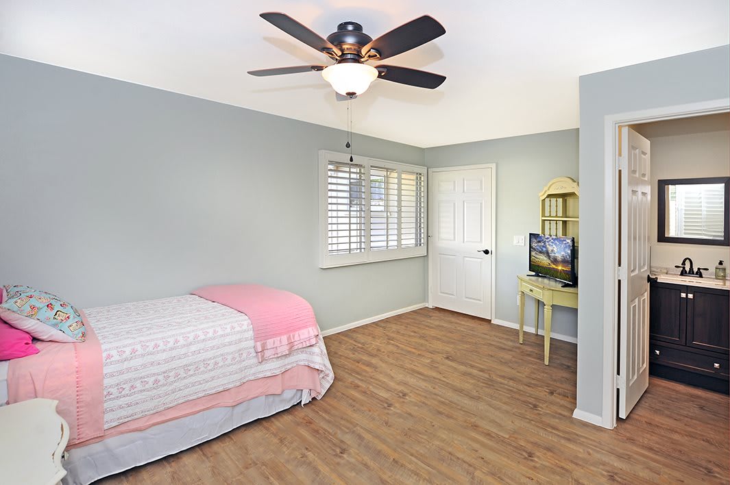 A simple, minimalist bedroom with a single bed, wooden floor, and ceiling fan.