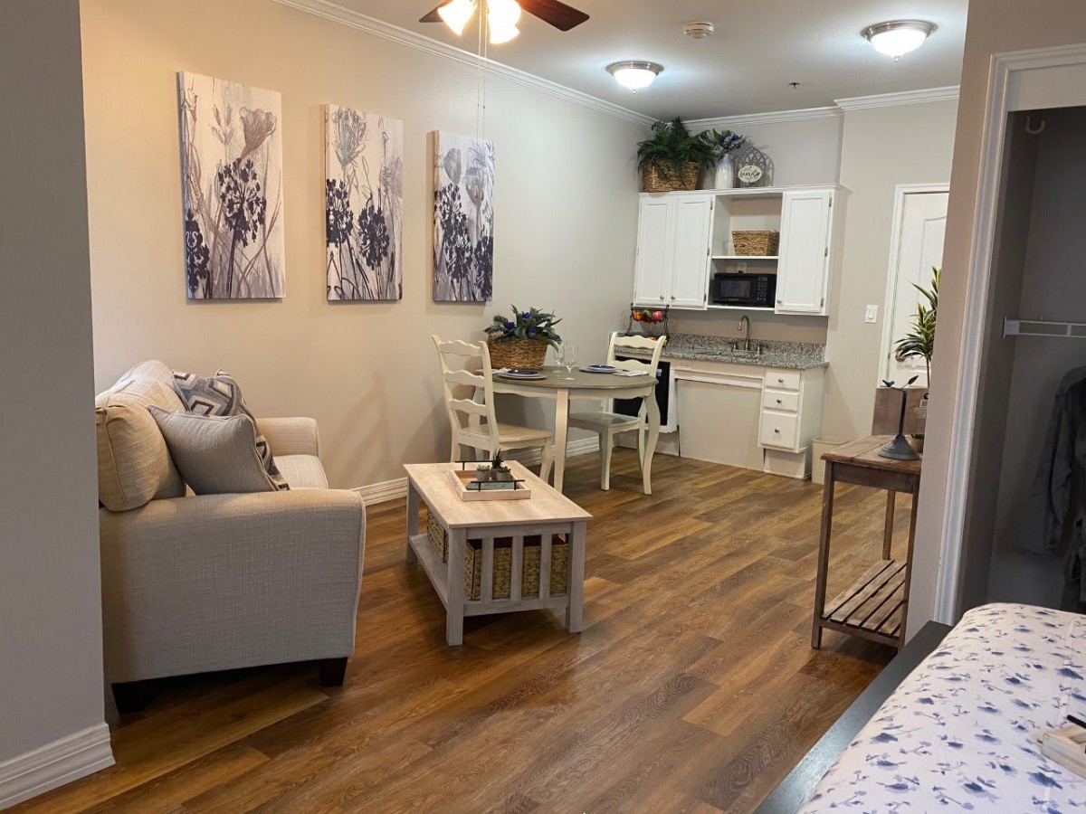 A cozy living area with wooden flooring, featuring a comfortable sofa, a small dining table, and modern kitchen space.